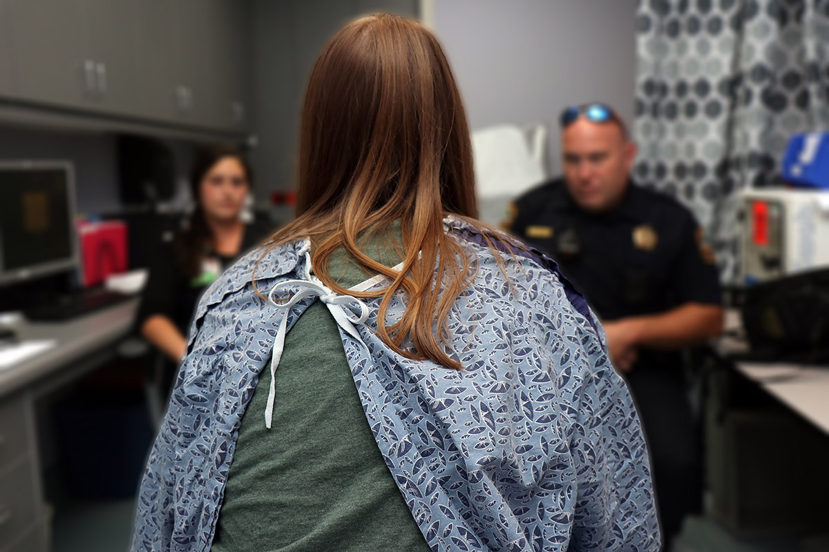 An unidentifiable sexual trafficking victim sits with her back to the camera and discusses the aftermath assault with members of law enforcement