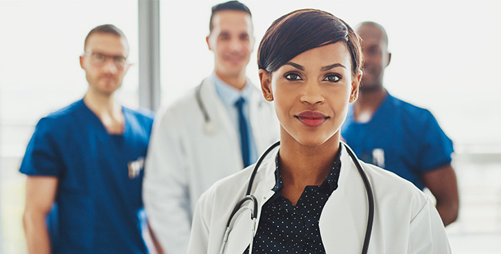 A female doctor stands in front of a group of three other healthcare professionals