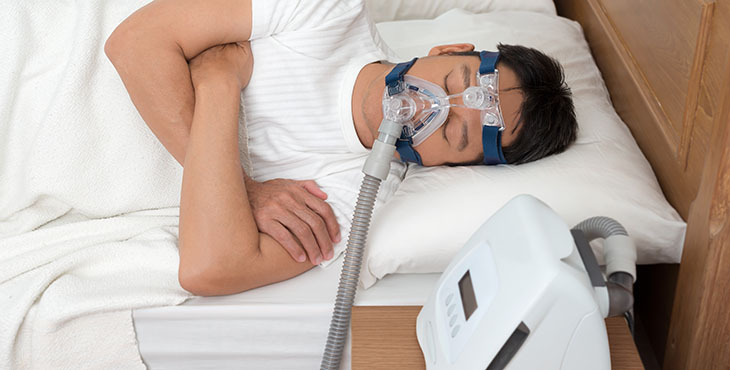 Man Wearing Cpap Mask While Suffering From Sleep Apnea On Bed At Home