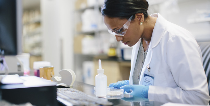 Female doctor examining petri dish at desk in medical room