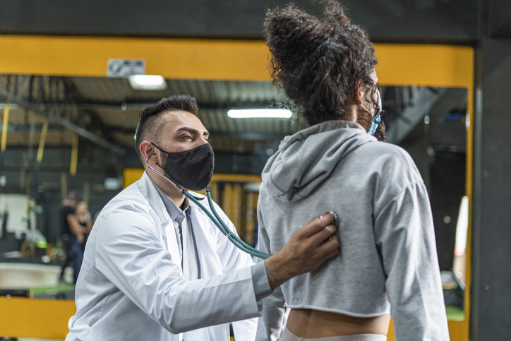 Doctor checks a young woman while doing sports in the gym wearing mask